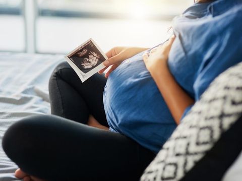 A photo with the focus on the unrecognizable pregnant woman in the foreground as the unrecognizable doctor shows her an ultrasound on a digital tablet in the background.