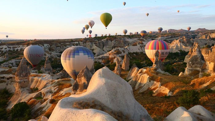 NEVSEHIR, TURKEY - AUGUST 10: Hot air balloons glide over historical Cappadocia region, located in Nevsehir province of Turkey  on August 10, 2021.  A total of 138,225 tourists enjoyed hot air balloon tours in TurkeyÃ¢s charming touristic hub Cappadocia between January and July. Cappadocia, listed as one of the UNESCO World Heritage places, is famous with its distinctive plateau, valleys, hills, unique fairy chimney volcanic cones, colorful frescos covering underground cities, boutique hotels, houses carved into rocks, rock churches, chapels, and shelters used by early Christians. (Photo by Behcet Alkan/Anadolu Agency via Getty Images)