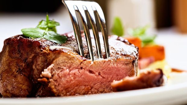 A fork pierces a juicy, succulent grilled fillet steak, grilled medium rare.