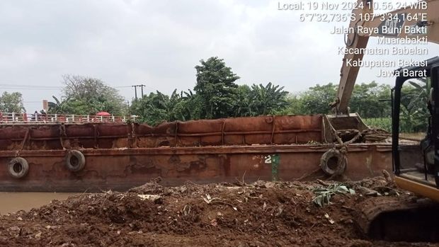 Penampakan kapal tongkang yang hanyut hingga tersangkut di jembatan Kali CBL, Babelan, Kabupaten Bekasi, Selasa (19/11/2024).