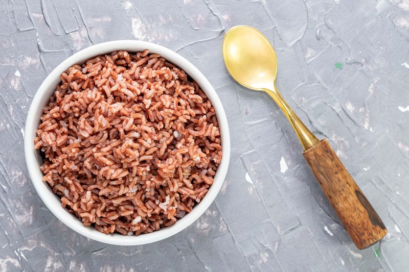 Rice red in bowl isolated on blue grey background has spoon close up, top view, Asian food and drink concept.