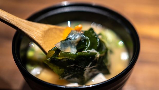 A bowl of Japanese miso soup filled with kelp and ingredients.