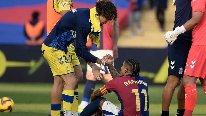 Barcelonas Brazilian forward #11 Raphinha (C) sits on the pitch as Las Palmas Portuguese forward #37 Fabio Silva shakes his hand after the Spanish league football match between FC Barcelona and UD Las Palmas at the Estadi Olimpic Lluis Companys in Barcelona on November 30, 2024. (Photo by Josep LAGO / AFP)