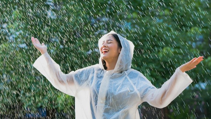 Ilustrasi jas hujan Rainy day asian woman wearing a raincoat outdoors. She is happy.