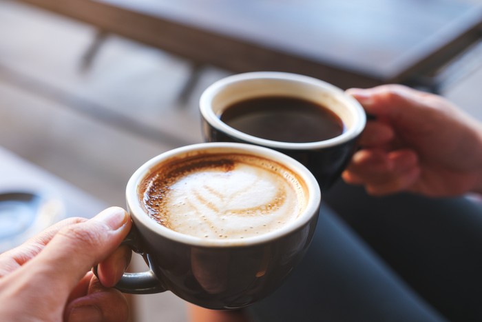 Ilustrasi kopi Closeup image of a man and a woman clinking white coffee mugs in cafe