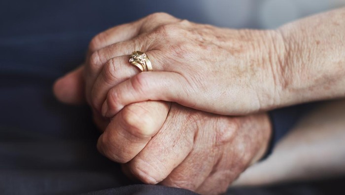 An elderly married couples hands, clasped tightly in affection.