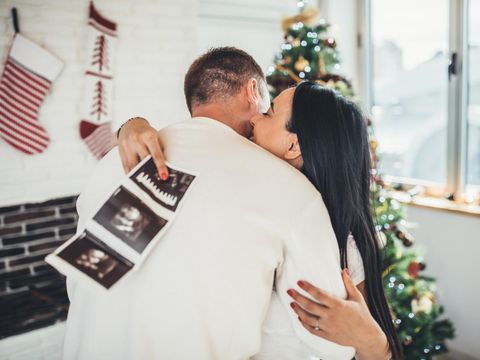 Happy pregnant woman with baby ultrasound photo embracing with her husband infront of the Christmas tree