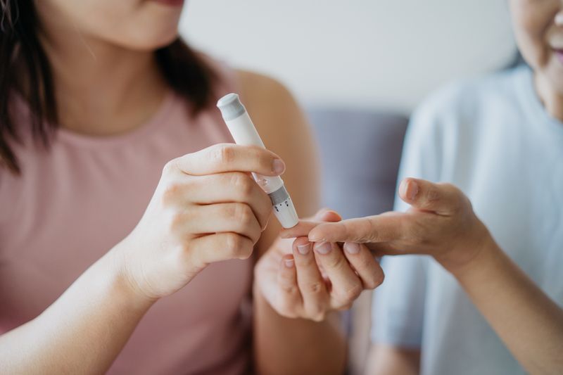 Image of an Asian Chinese woman helping her mother check blood sugar level using a blood glucose meter at home