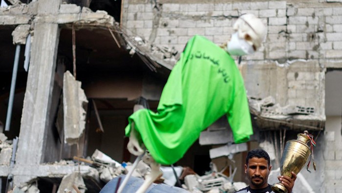 A son of Palestinian soccer player Ahmed Al-Loulahi holds a trophy retrieved from their destroyed house, with his father's jersey hanging, amid a ceasefire between Israel and Hamas, in Rafah in the southern Gaza Strip, January 22, 2025. REUTERS/Mohammed Salem