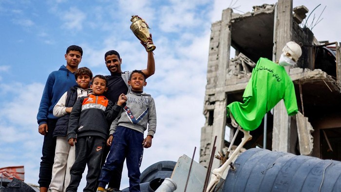 A son of Palestinian soccer player Ahmed Al-Loulahi holds a trophy retrieved from their destroyed house, with his father's jersey hanging, amid a ceasefire between Israel and Hamas, in Rafah in the southern Gaza Strip, January 22, 2025. REUTERS/Mohammed Salem