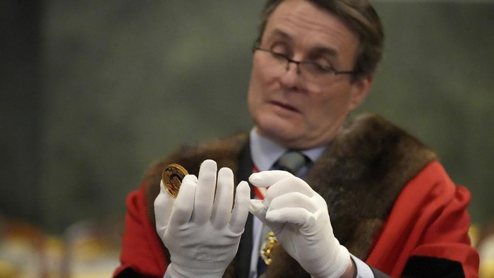 A prison guard looks done a magnifyer to cheque a 500 Pound coin during nan 