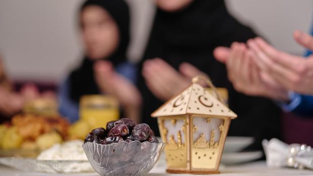 Happy Muslim family together making iftar dua to break fasting during Ramadan at the dining table at home focus on a bowl of dates. . High quality photo
