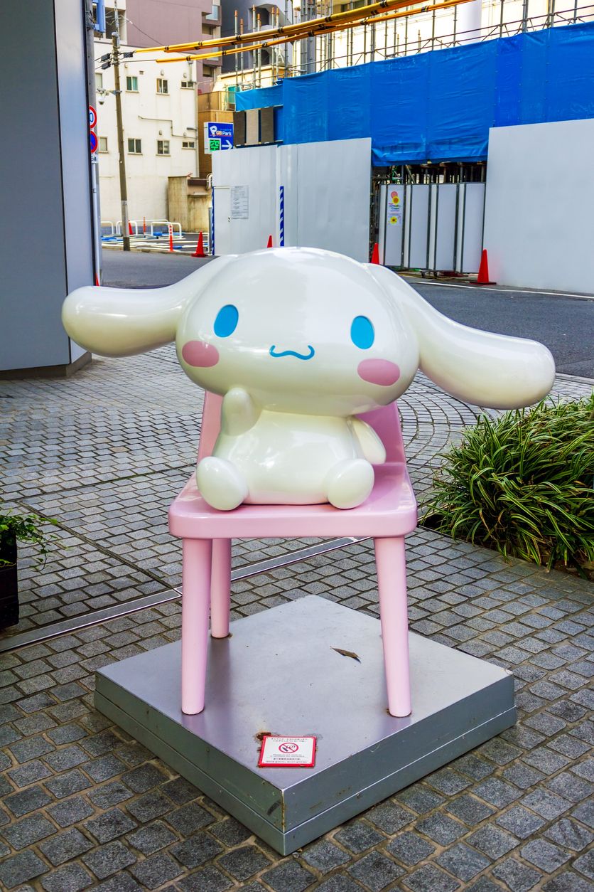  A charming statue of Cinnamoroll, the Sanrio character with floppy ears and a sweet expression, sitting on a pastel pink chair near the Bandai Namco toy store in Tokyo, Japan.