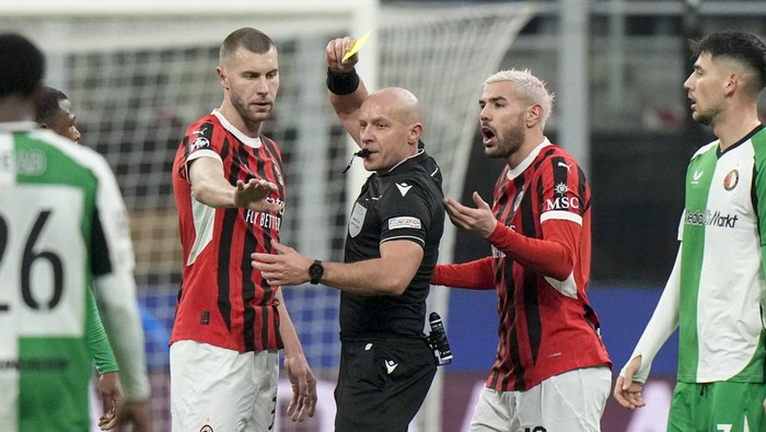 Referee Szymon Marciniak of Poland shows the yellow card to AC Milans Theo Hernandez, right, during Champions League, playoff second leg soccer match between AC Milan and Feyenoord, at the San Siro stadium in Milan, Italy, Tuesday, Feb.18, 2025. (AP Photo/Luca Bruno)