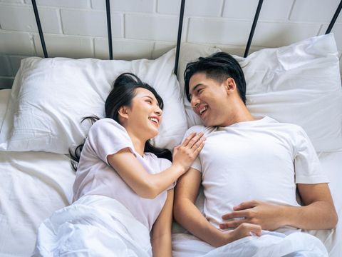 A happy young Asian couple in pajamas is enjoying watching television or a movie together in bed. couple and domestic life concepts