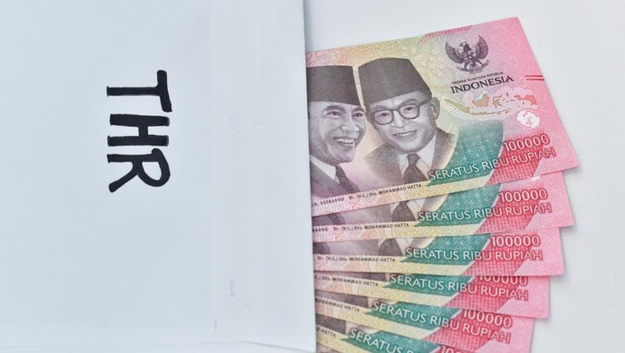 Ilustrasi Pencairan THR ASN 2025 dengan uang rupiah di amplop THR, menunjukkan IDR 100.000 tunai. THR adalah tunjangan yang diberikan kepada ASN, TNI, dan Polri untuk Lebaran.