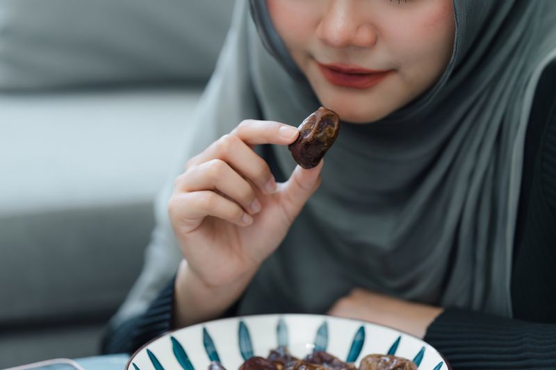 Muslim woman in hijab eating dates fruit in a comfortable home. Clouse up shot