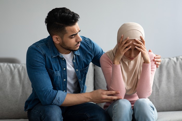 Middle-eastern bearded man comforting his crying wife, young muslim couple having problems in relationships, visiting family therapist together. Frustrated lady in hijab feeling unhappy
