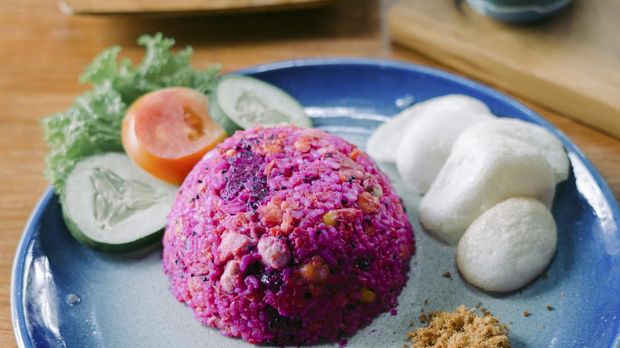 Pink fried rice made from dragon fruit served with tempeh, kerupuk crackers, chicken floss, and vegetables