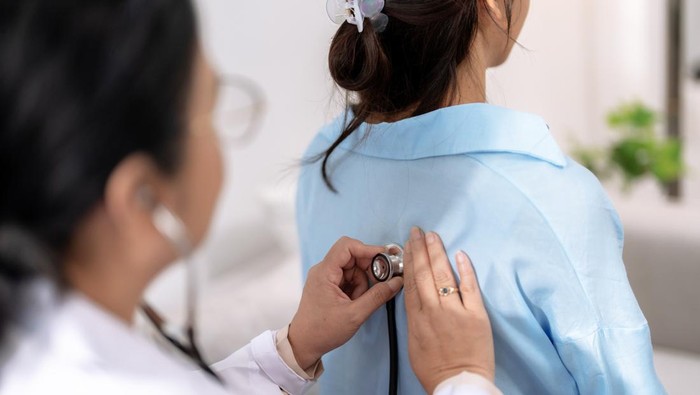 Ilustrasi Cek Kesehatan Gratis Doctor uses stethoscope to listen to the lungs of a female Asian patient to determine symptoms and provide treatment.