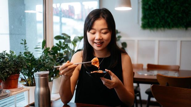 Asian woman holding a piece of kimchi with Korean metal chopsticks