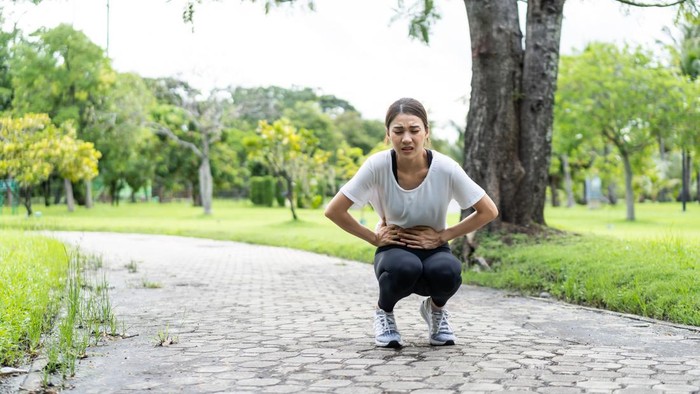Asian attractive sport woman feels pain on stomach after run on street. Beautiful girl in sportswear having stomach ache illness while exercise by jogging workout outdoor in the evening in public park