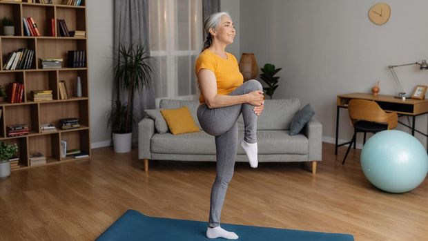 Domestic fitness. Fit senior woman in sportswear doing exercises on yoga mat, stretching her leg on home workout, leading active lifestyle, free space
