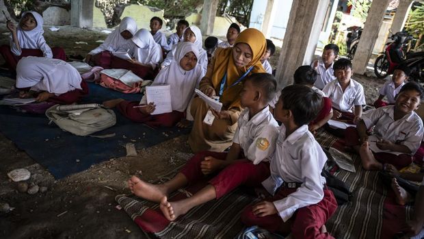 Guru kelas 3 Indah (tengah) menyampaikan materi kepada muridnya di kolong bangunan SD Negeri Bendono 1, Sayung, Kabupaten Demak, Jawa Tengah, Senin (5/5/2025). Menurut Komite Sekolah setempat, gedung baru SDN Bedono 1 yang dibangun sebagai relokasi proyek Tol Laut Semarang-Demak seharusnya sudah dapat digunakan, namun seluruh ruangannya masih terkunci oleh kontraktor, sehingga kegiatan belajar mengajar terpaksa dilakukan di kolong bangunan. ANTARA FOTO/Aprillio Akbar/bar