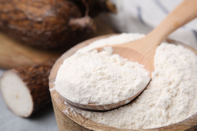 Wooden bowl and spoon with cassava flour on table, closeup
