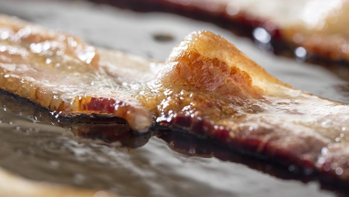 681154774 Macro of strips of bacon cooking in a frying pan.