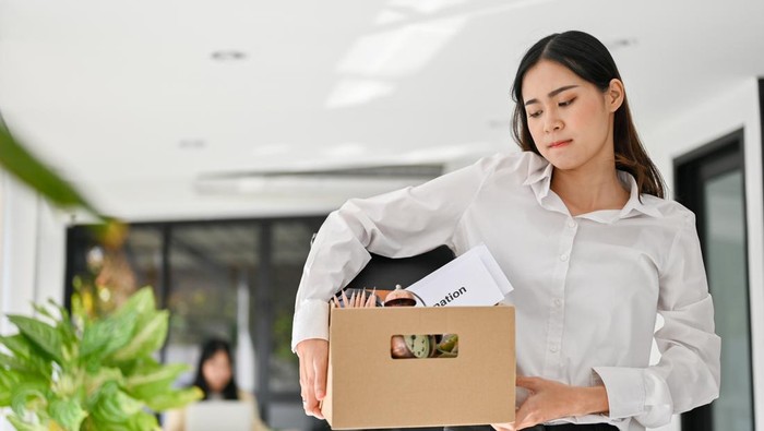 Ilustrasi PHK atau resign Sad and upset young Asian female office worker carrying her belonging, quitting a job, being fired from her boss.