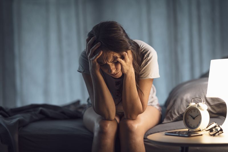 Depressed woman sitting on the bed at night, she is sad and suffering from insomnia