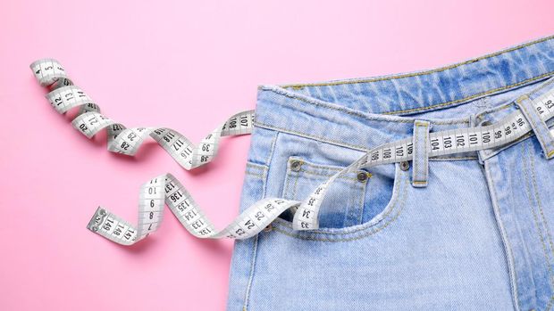 Jeans and measuring tape on pink background, top view