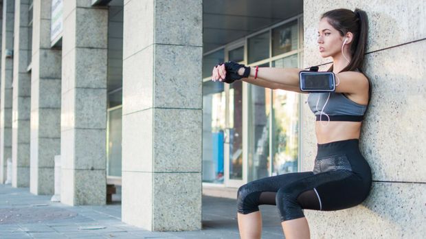 Young sporty girl doing wall sitting exercise urban outdoors.