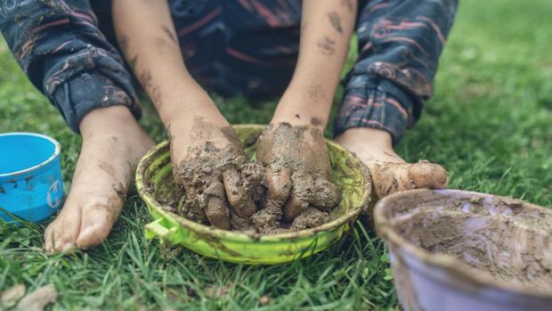 Retro image of toddler child sitting in grass playing with mud having his hands and feet all dirty.