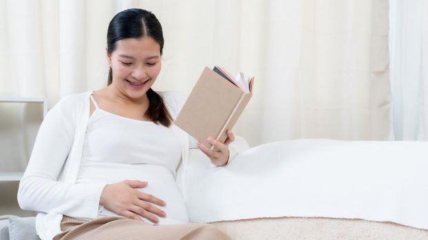 Pregnant woman reading a stories to her unborn child in the living room at home