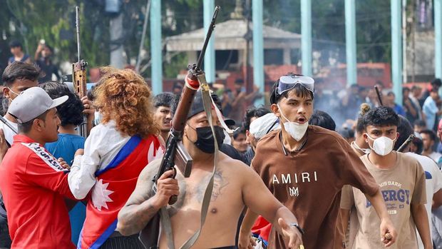 A protester carries a firearm as demonstrators gather outside the Singha Durbar palace complex during a protest to condemn the police's deadly crackdown on demonstrators in Kathmandu on September 9, 2025, a day after demonstrations over social media prohibitions and corruption by the government. Nepal rolled back its social media ban on September 9, a day after at least 19 people were killed in youth protests demanding that the government lift its restrictions and tackle corruption. Protests continued on September 9, defying a curfew to vent anger at one of the deadliest crackdowns on demonstrators for years -- despite all major social media apps resuming operations online and the government appealing for calm. (Photo by Prabin RANABHAT / AFP)