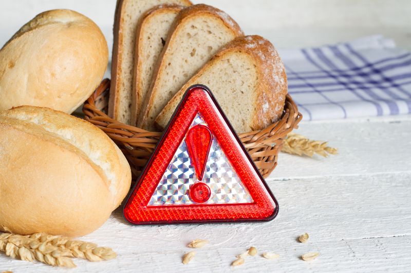 Gluten intolerance with bread wheat and warning sign on white planks closeup