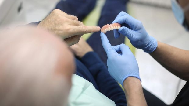 Senior man at a dentist's office, looking at dentures. About 65 years old, Caucasian male.