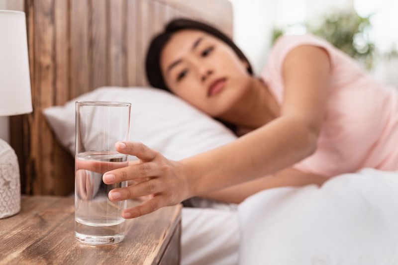 Healthy Liquid. Asian Lady Drinking Water From Glass Starting Day With Hydration Lying In Bed At Home. Selective Focus