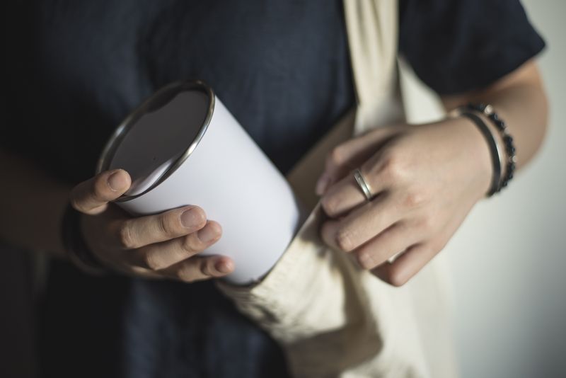 Young woman bringing and taking out tumbler, reusable coffee mug/cup from her bag.