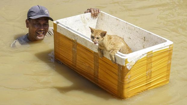 A man wades through neck-deep floodwaters with a rescued cat in a styrofoam box in Kuala Simpang village in Aceh Tamiang, North Sumatra on November 30, 2025. Officials in Indonesia and Sri Lanka battled December 3 to reach survivors of deadly flooding in remote, cut-off regions as the toll in the disaster that hit four countries topped 1,300. (Photo by IWAN GUNADI BATUBARA / AFP)