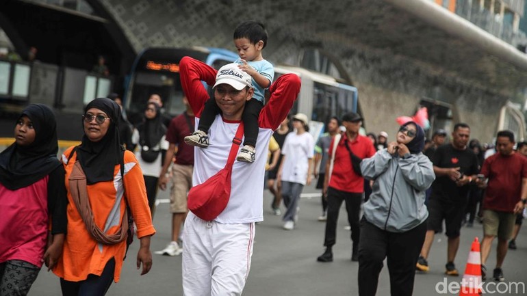 Warga menikmati jalan santai, memanfaatkan momen CFD untuk relaksasi dan menjaga kebugaran. Pemandangan gedung-gedung tinggi menjadi latar aktivitas warga.