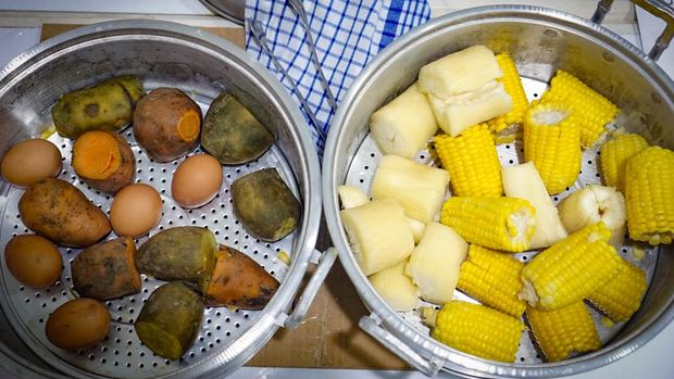 A pot of boiled food contains several ears of corn on the cob, sweet potatoes and eggs.