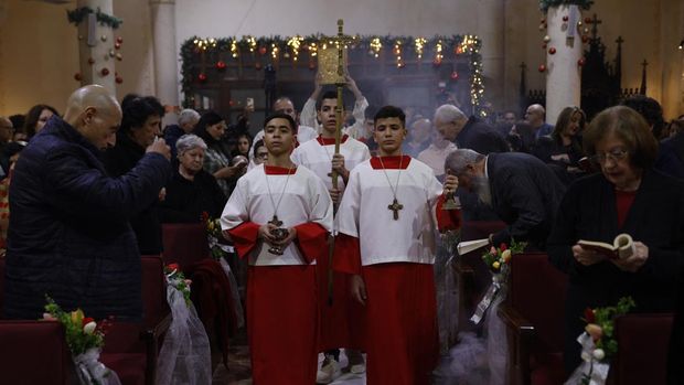 Alter servers and the cross bearer walk down the aisle during a Christmas mass celebrated with displaced worshippers at the Roman Catholic Church of the Holy Family in Gaza City on December 24, 2025. The majority of Gaza's 2.4 million people have been displaced, often multiple times, by the war that began with Hamas's attack on southern Israel on October 7, 2023. With many displaced living in tent camps, the coming winter is raising serious concerns. (Photo by Omar AL-QATTAA / AFP)