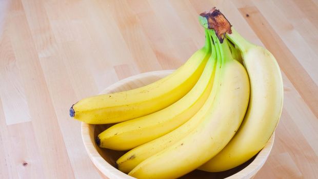 Bunch of bananas in a wooden bowl on a table.