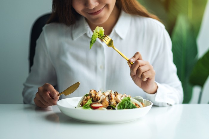 Closeup image of a young woman eating chicken salad on table in the restaurant