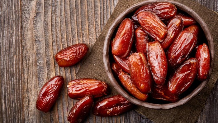 Bowl of dried dates on wooden background from top view