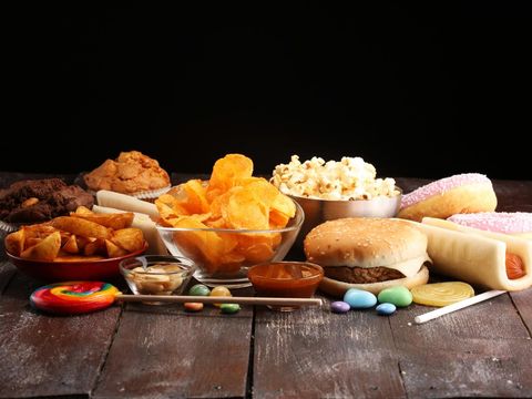Woman reaching for a donut from a table full of junk food, showing signs of sugar cravings, overeating, and unhealthy eating habits