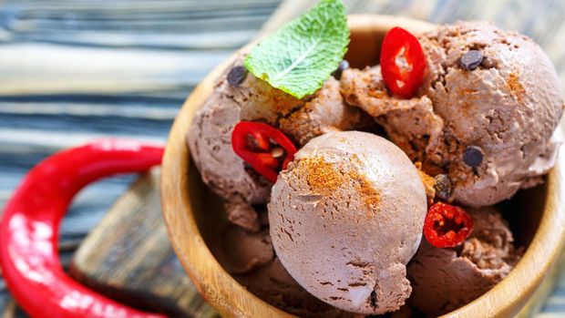 Delicious chocolate ice cream with chili peppers in a wooden bowl closeup, selective focus.